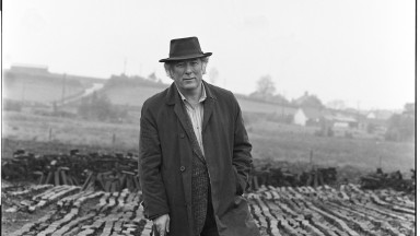 Black and white photo of man standing at turf bog. 