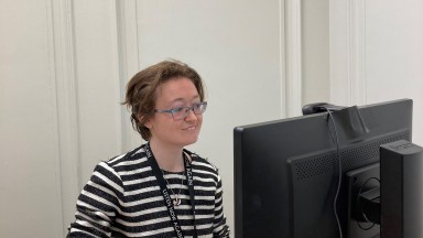 Grianghraf de bhean le spéaclaí ag féachaint ar ríomhaire.