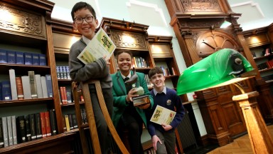 George Pham, Ellie Reynolds and Shay Collins standing on ladder in the NLI's Reading Room