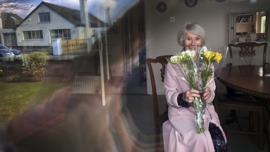 Older woman behind window holding a bunch of flowers