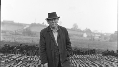 Seamus Heaney standing in the bog leaning on a wooden walking stick