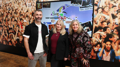 A man and two women in front of a photo of a concert