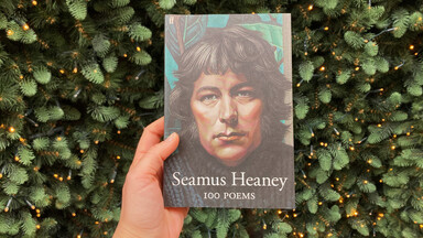 A hand holding up Heaney's 100 poems in front of Christmas lights