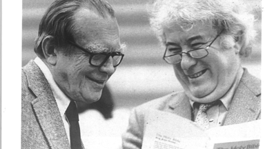 A black-and-white photograph of poets Czesław Miłosz and Seamus Heaney smiling together in conversation.