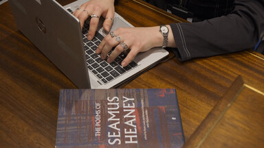 an image showing someone working on a laptop next to a book of Seamus Heaney's poems