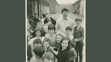 Heaney as a young man standing on the street surrounded by school children