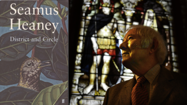 A portrait of Seamus Heaney standing in front of a stained-glass window, looking upwards. Beside him is the cover of his poetry collection District and Circle, featuring an illustrated bird among leaves.