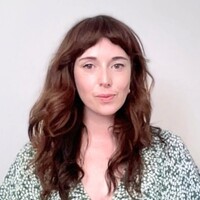 Portrait of Ann Marie Duffin with long, wavy auburn hair and a green-and-white patterned blouse, against a plain light background.