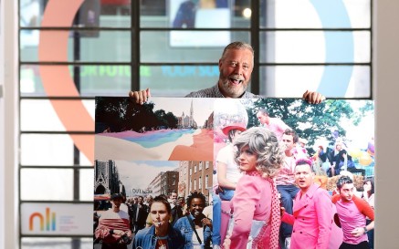 A man holds up an enlarged photograph of a Pride parade