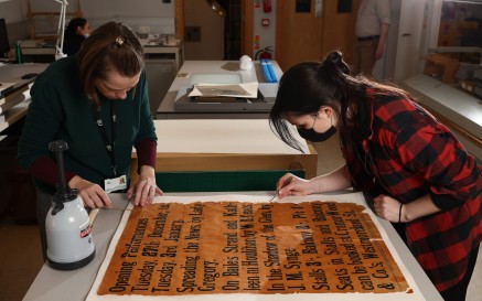 Two people working on conserving an old poster