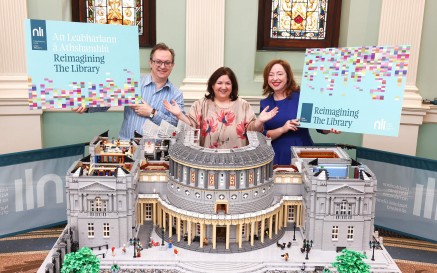 Triúr ina seasamh taobh thiar de mhionsamhail Lego den Leabharlann Náisiúnta