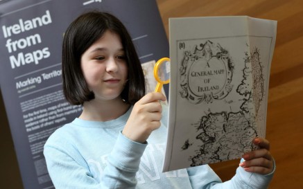 A young girl uses a yellow magnifying glass to examine a historic map. 
