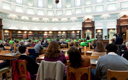 Visitors are seated in the Reading Room at the National Library of Ireland, watching a woman speak during a Poetry Aloud event 