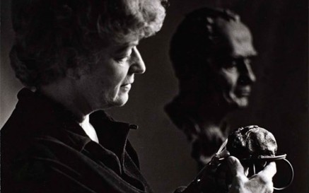 A black and white photo of Helen Hooker O'Malley holding a sculpture, with a bust in the background woman
