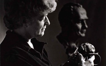 A black and white photo of Helen Hooker O'Malley holding a sculpture, with a bust in the background woman 