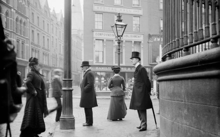 Men and women of Dublin stand on the footpath at the junction of Suffolk Street, Grafton Street and Nassau Street. 