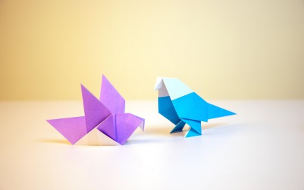 A purple and blue origami bird on a white table 