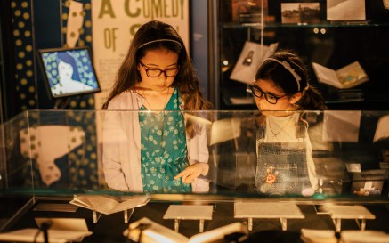 Two young girls wearing glasses examine exhibition materials in a glass case