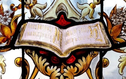 A portion of stained glass featuring an open book surrounded by ornate decorations 