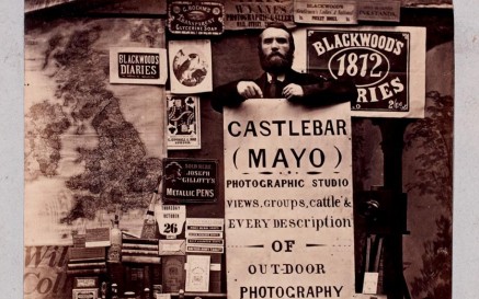 Sepia photograph of a man holding a large sign advertising his Photographic Studio in Castlebar, Co.Mayo