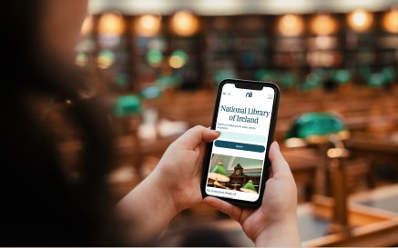 Close up a woman holding an iPhone browsing the NLI's website inside of the Reading Room