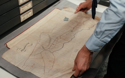 man handling a historical map laid out on a table 