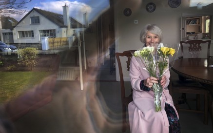 Older woman behind window holding a bunch of flowers