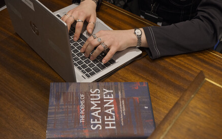 an image showing someone working on a laptop next to a book of Seamus Heaney's poems