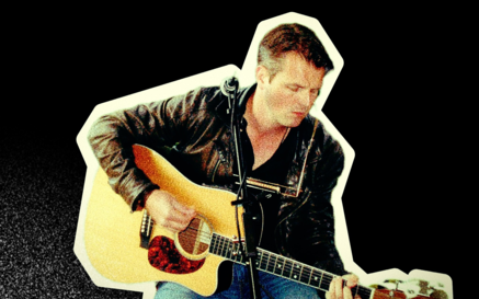 A musician sitting and playing an acoustic guitar, wearing a black leather jacket and jeans, with a microphone positioned in front of him. The image has a vintage, grainy appearance with a cream-coloured cut-out border against a black background.