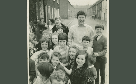 Heaney as a young man standing on the street surrounded by school children